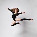 Young girl gymnast in black sport body and uppers jumping and making dymnastic pose in air over white background