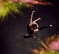 Young girl gymnast in black sport body and uppers making circle in jump over dark background with colorful glittering Royalty Free Stock Photo