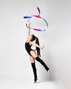 Young girl gymnast in black sport body and uppers standing and making exercise with gymnastic tape over white background