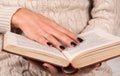 Young Girl hand with black nails holds book, woman in sweater reading book Royalty Free Stock Photo