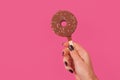 Female hand with doughnut ice cream on a stick on pink background in studio