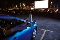 Young girl hanging her legs out of car window while watching a movie at drive in cinema from the front seat of the car Royalty Free Stock Photo