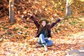 Young girl in hat and autumn clothes playing with golden fall leaves in hand. Happy girl in hat and plaid jacket on an autumn