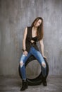 Young slim girl sitting on a car tire on the background of gray concrete wall Royalty Free Stock Photo