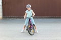 Young girl with a helmet sitting on a bike ready to go, in front of a textured brown gate, confident child cyclist, biker, central Royalty Free Stock Photo