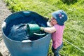 Young girl helping in the vegetable garden and fills a large watering can in a blue barrel