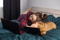 Young girl and her dog french bulldog working in bed at a laptop during quarantine Royalty Free Stock Photo