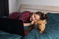 Young girl and her dog french bulldog working in bed at a laptop during quarantine Royalty Free Stock Photo