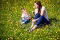 Young girl and her mom sitting on meadow, smelling flowers, family time, blurred background Royalty Free Stock Photo