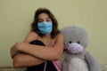 Young girl with her teddy bear peluche both wearing a medical mask during Covid19 infection