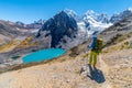 Girl hiking by stunning lake Juraucocha, San Antonio pass with view to Siula Grande peak, Huayhuash range, Huaraz, Ancash, Peru