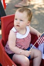 Young girl holding an American flag and riding in red wagon having fun in the park for July Fourth Royalty Free Stock Photo