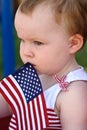 Young girl holding an American flag and riding in red wagon having fun in the park for July Fourth Royalty Free Stock Photo