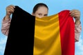 Young girl holding in both hands the national flag of Belgium on beautiful shiny silk against a blue sky, state concept, travel,
