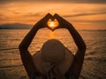 Young girl holding hands in heart shape framing setting sun at sunset Royalty Free Stock Photo