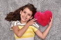 Young girl holding red plush heart lying on the carpet Royalty Free Stock Photo