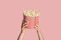 Young girl holding striped bucket with popcorn on pink background, closeup view Royalty Free Stock Photo