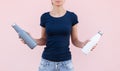 Young girl holding two reusable, steel thermo water bottles, white and grey of colors. Pastel pink background. Be plastic free.