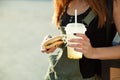 A young girl holds a drink and a cheeseburger in the hand, again