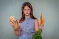 A young girl holds fresh carrots in one hand and shawarma in the other, looks at the shawarma and cannot decide which is healthier