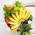 Young girl holds full paper bag of groceries over white wooden surface, top view. Overhead, from above Royalty Free Stock Photo