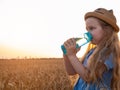 Young girl holds reusable bottle in hands drinks water in wheat field. Pure mineral water advertisement.Active lifestyle. Royalty Free Stock Photo