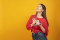 Young girl holds wad of money with pensive dreamy face on yellow background. Career growth and high salaries for young people.