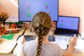 Young girl at home looking at two screens of desktop computer, rear view. Back to school, homeschooling, distance