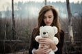 Young girl hugs a teddy bear on the background of burnt forest