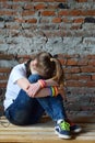 Young girl in jeans and white T-shirt is sitting on the floor and crying. Concept of a non happy and sad teenager Royalty Free Stock Photo