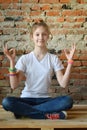 Young girl in jeans and white T-shirt is sitting on the floor and meditates. Concept portrait of a pleasant friendly happy Royalty Free Stock Photo