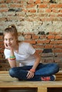 Young girl in jeans and white T-shirt is sitting on the floor and smiling. Concept portrait of a pleasant friendly happy teenager Royalty Free Stock Photo
