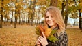 A young girl joyfully posing on the camera with a bouquet of colorful leaves. Walk in the city park in the autumn.