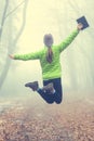 Young girl jumps up with her hands up - Active modern lifestyle - tablet in hand - magic misty forest in autumn mountains.