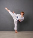 A young girl karateka in white kimono and a blue belt trains and performs a set of exercises against a gray wall Royalty Free Stock Photo