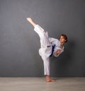 A young girl karateka in white kimono and a blue belt trains and performs a set of exercises against a gray wall Royalty Free Stock Photo