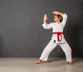 Young girl karateka in a white kimono and a red belt trains and performs a set of exercises against a gray wall Royalty Free Stock Photo