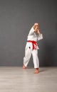 Young girl karateka in a white kimono and a red belt trains and performs a set of exercises against a gray wall Royalty Free Stock Photo