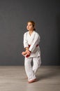 Young girl karateka in a white kimono and a red belt trains and performs a set of exercises against a gray wall Royalty Free Stock Photo