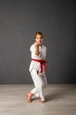 Young girl karateka in a white kimono and a red belt trains and performs a set of exercises against a gray wall Royalty Free Stock Photo