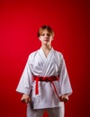 Young girl karateka in a white kimono and a red belt trains and performs a set of exercises on a bright red background Royalty Free Stock Photo