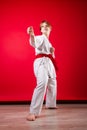 Young girl karateka in a white kimono and a red belt trains and performs a set of exercises on a bright red background Royalty Free Stock Photo