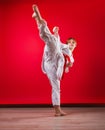 Young girl karateka in a white kimono and a red belt trains and performs a set of exercises on a bright red background Royalty Free Stock Photo