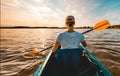 Young girl in a kayak paddling on the lake at sunset - view from behind her back Royalty Free Stock Photo