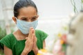 Young girl kid in medical mask praying to god to protect from coronavirus or covid-19 by folding hands in namaste Royalty Free Stock Photo