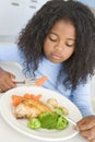 Young girl in kitchen eating chicken and vegetable