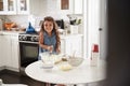 Young girl in the kitchen making cake mixture on her own, looking to camera