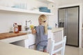 Young girl kneeling on chair washing up, back view Royalty Free Stock Photo