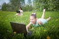 Young girl with laptop resting on a green lawn or a field in a park in nature and her mon on the background. Fmily with Royalty Free Stock Photo