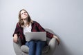 Young girl with a laptop sitting on a soft comfortable chair and thinking, a woman using a computer against a white blank wall, Royalty Free Stock Photo